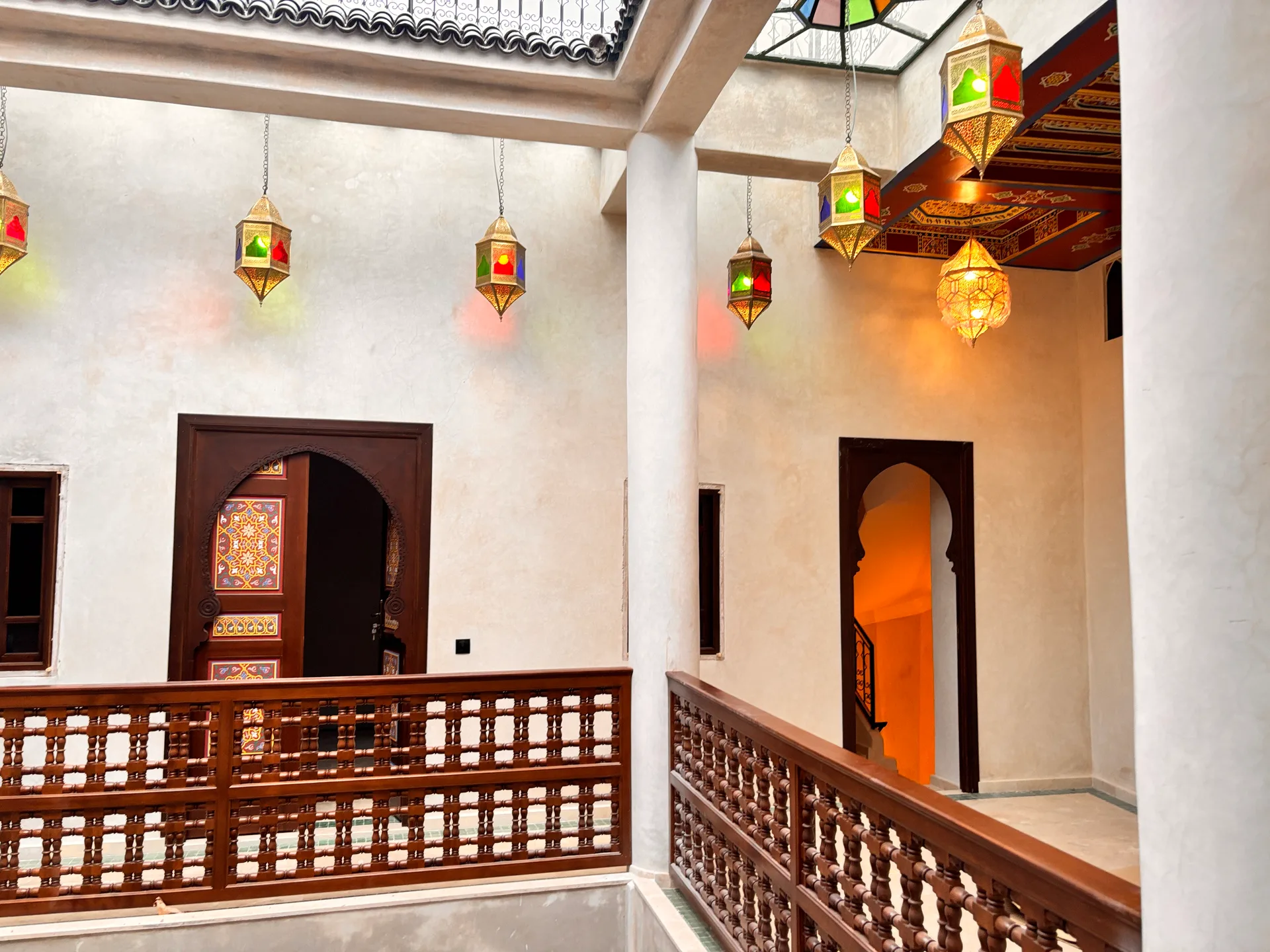 Riad Hantata gallery — Moroccan lanterns casting warm colored light under stained glass and carved cedar ceiling